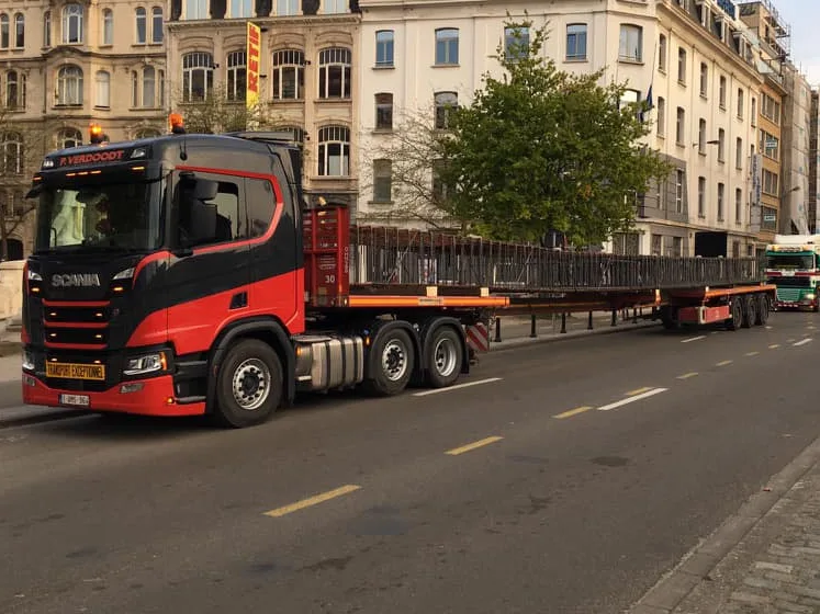 Zwart-rode Scania van P. Verdoodt met een meters lange stalen vakwerkligger op een verlengbare oplegger door een stadsstraat
