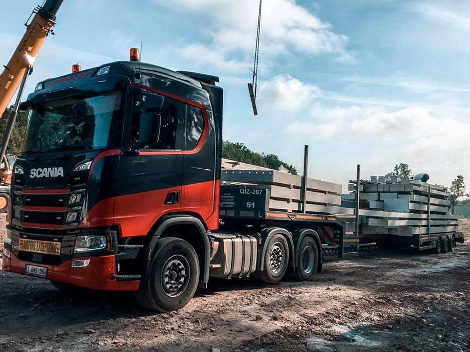 P. Verdoodt Scania met dieplader-oplegger op een bouwwerf, kraan-haak in beeld tijdens het lossen van prefab-elementen
