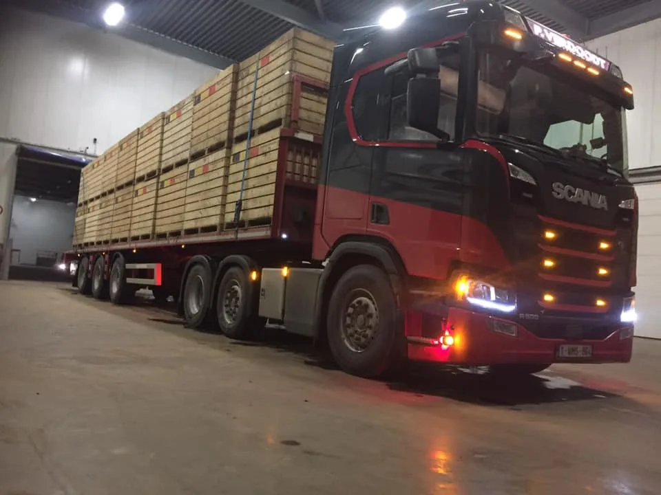Oplegger met houten kratten wordt bij avond geladen in het depot van P. Verdoodt